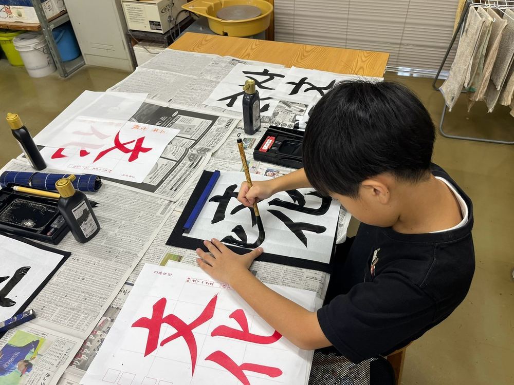 A child writing 「文化」 (“culture”) with a brush