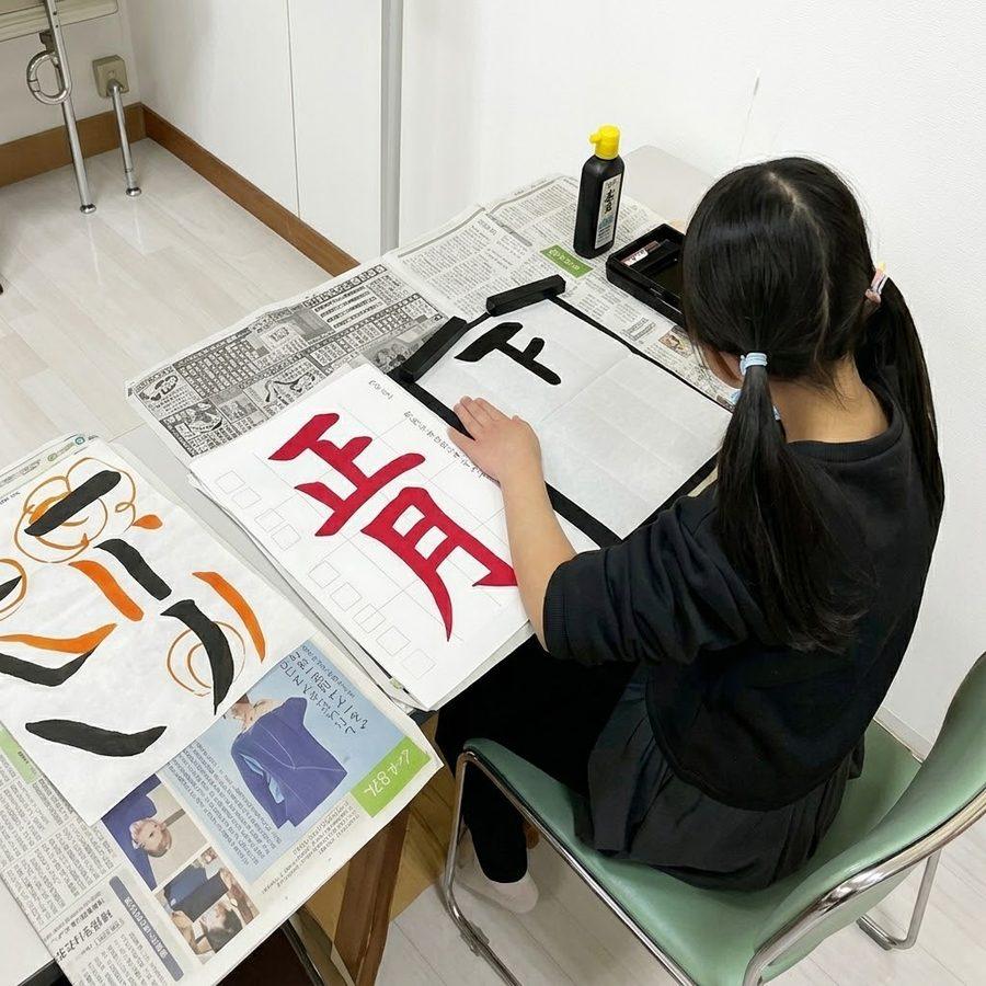 お手本を見ながら、筆で字を書く女の子