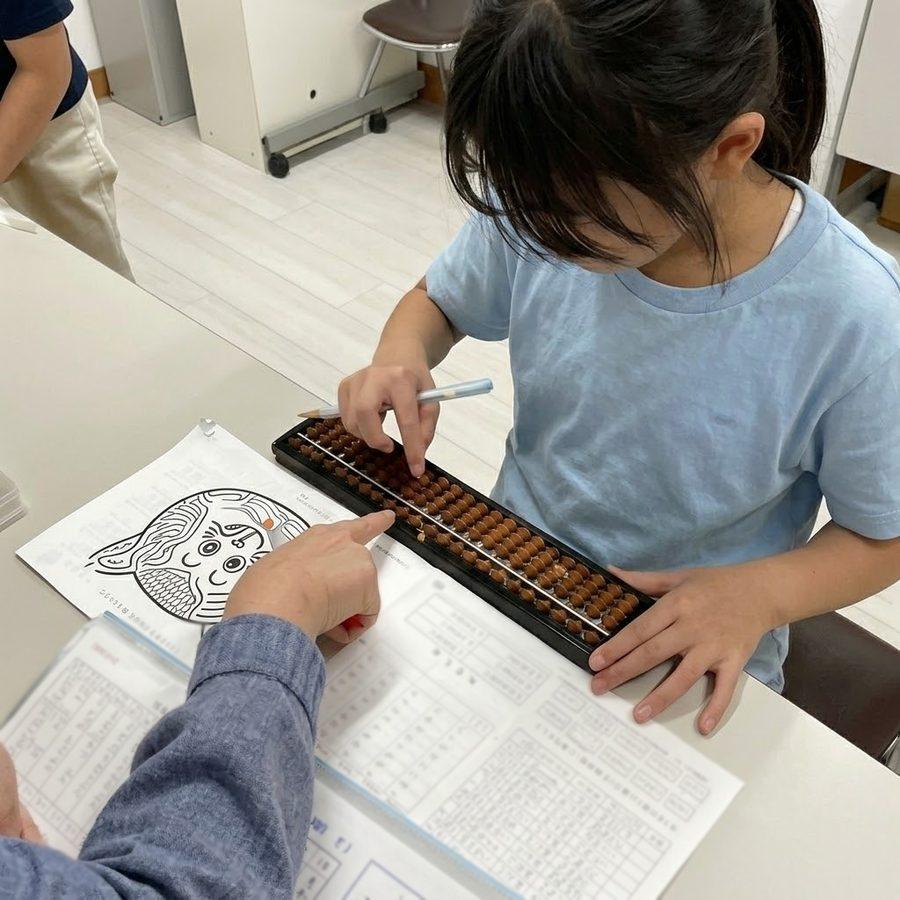 先生と一緒に、そろばんの珠を指で動かす女の子